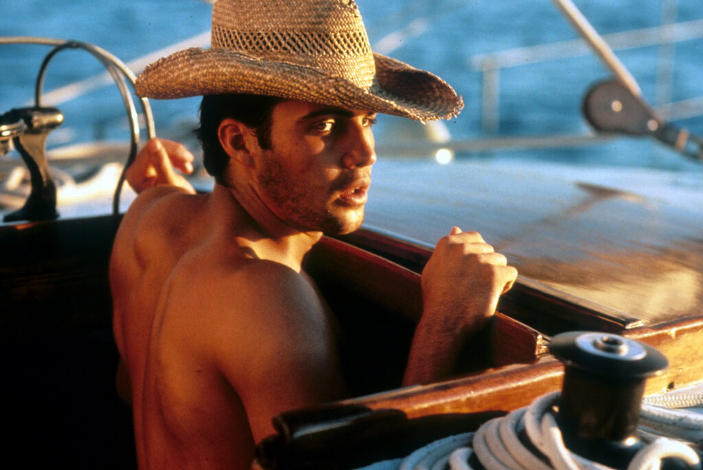 Billy Zane in a boat shirtless with a hat on in a scene from the film Dead Calm